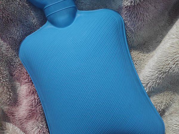 Symbolbild: Blaue Wärmflasche auf einer flauschigen Decke